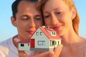 Young Woman And Man Keeping In Hands Model Of House With Garage